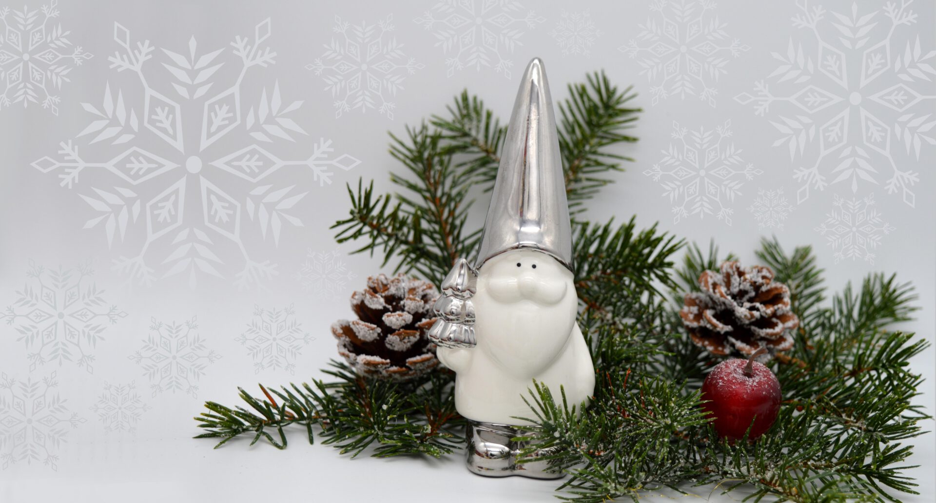christmas-motif-6723208 Weihnachtliches Motiv mit Tannenzweigen, Tannenzapfen und einer kleinen Weihnachtsfigur in silber/weiß. Hintergrund in weiß, grau mit Sternenmuster.